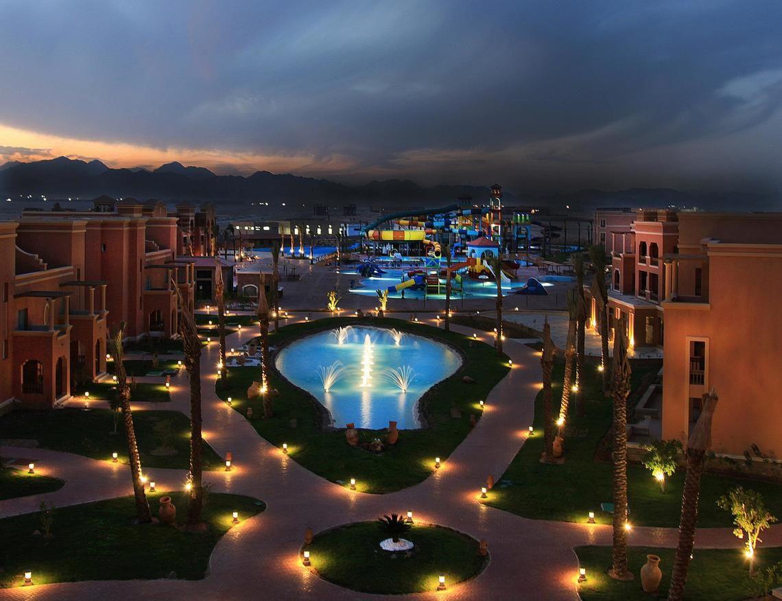 Charmillion Club Aqua Park Außenbereich bei Nacht mit Wasserrutschen, Brunnen und beleuchteten Wegen.