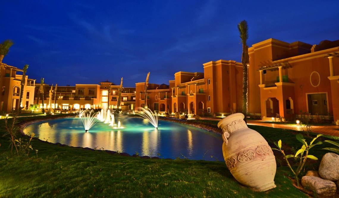 Charmillion Club Aqua Park bei Nacht mit beleuchtetem Wasserbrunnen und Gebäuden.