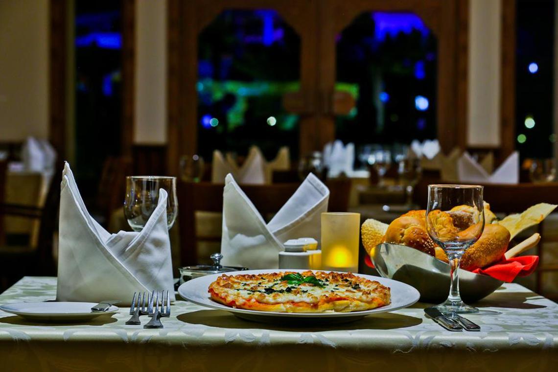 Im Charmillion Club Aqua Park ein Tisch mit einer Pizza, Gläsern und Brötchen.