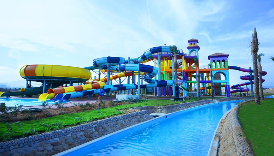 Farbige Wasserrutschen im Charmillion Club Aqua Park neben einem großen Schwimmbecken.