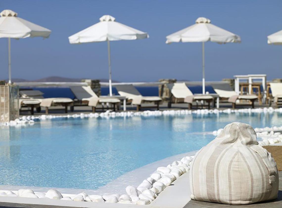 Pool im Rocabella Mykonos Art Hotel mit Sonnenliegen und Sonnenschirmen am Rand.