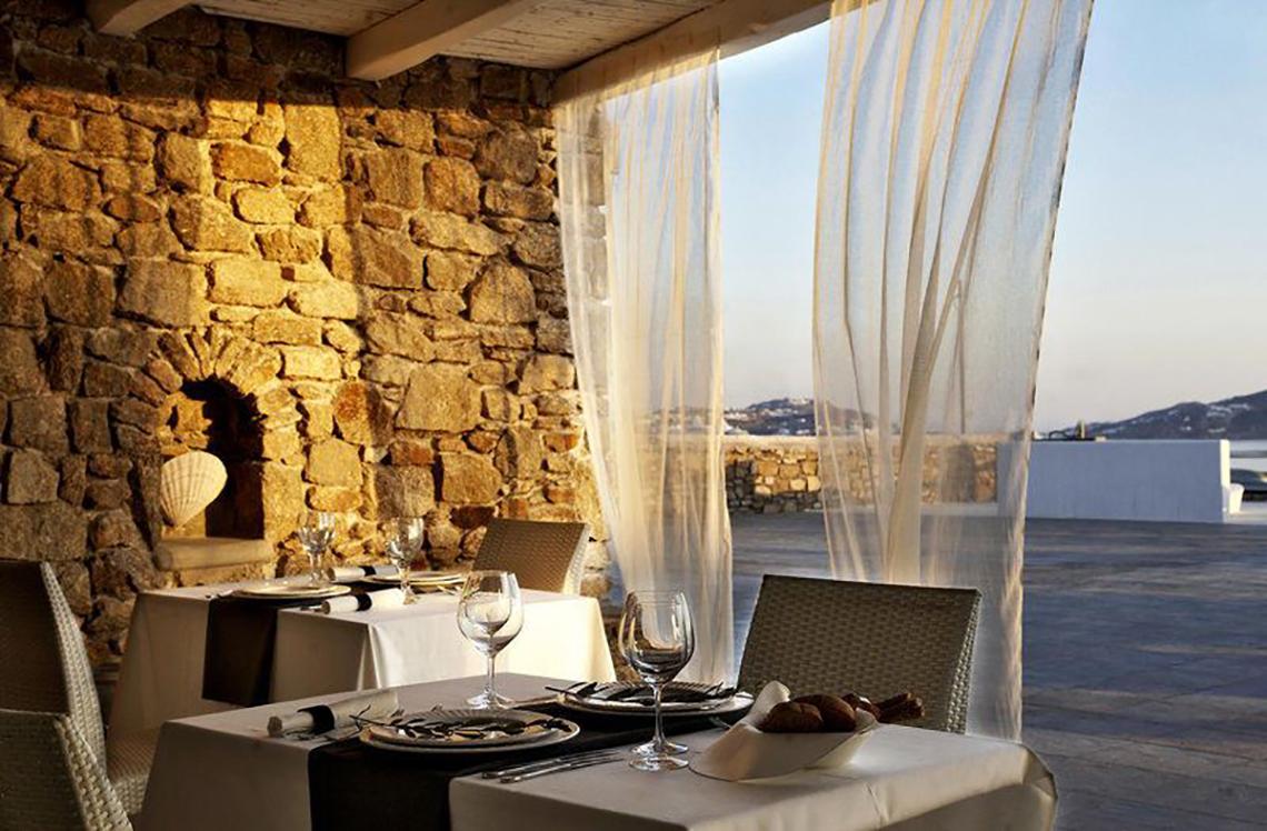 Außenterrasse des Rocabella Mykonos Art Hotel & Spa mit gedeckten Tischen und Blick auf die Umgebung.