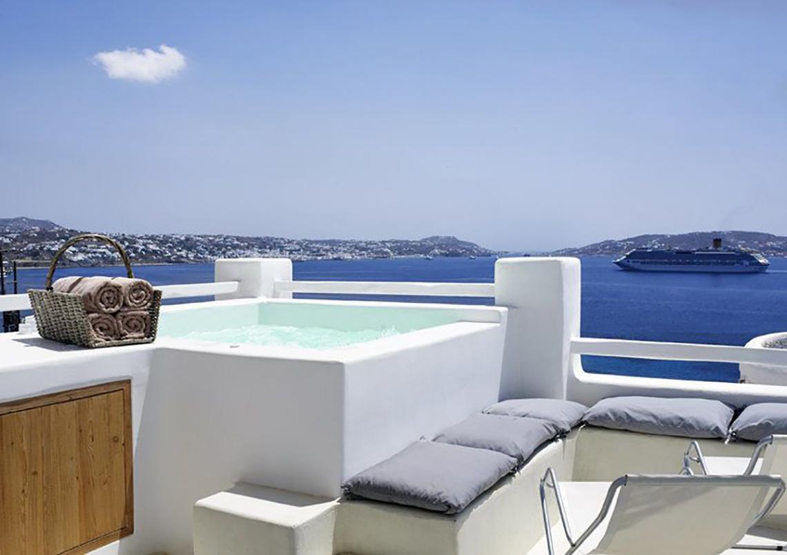 Balkon des Rocabella Mykonos Art Hotel & Spa mit Whirlpool und Blick auf das Meer und eine Kreuzfahrt.