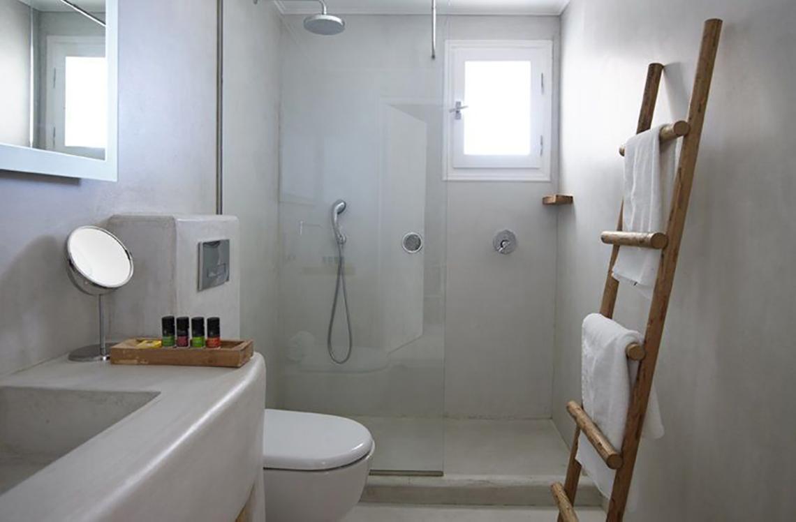 Badezimmer im Rocabella Mykonos Art Hotel mit Glasdusche, Toilette, Waschbecken und Holzleiter.