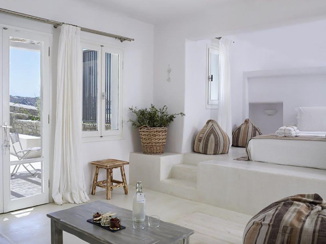 Inneneinrichtung des Rocabella Mykonos Art Hotel mit weißen Wänden, einem Bett, einem Tisch und einem Korb mit einer Pflanze.