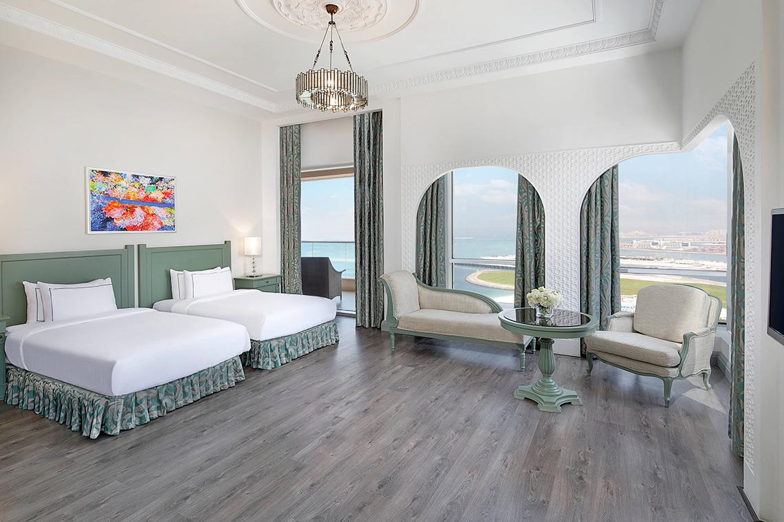 Innenansicht der Suite im Habtoor Grand Resort & Spa mit zwei Betten, Sofa und Blick auf das Meer.