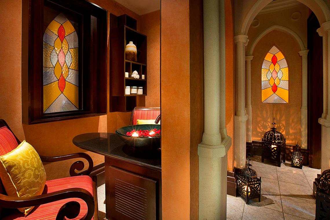 Innenansicht des Habtoor Grand Resort & Spa mit gemusterten Fenstern, einem Tisch mit Rosenblättern und illuminierten Laternen.