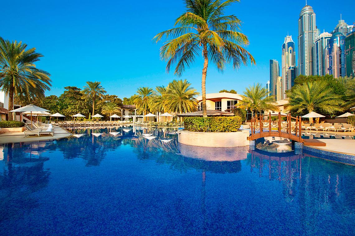 Ein großer Swimmingpool im Habtoor Grand Resort & Spa mit Palmen und Sonnenschirmen.