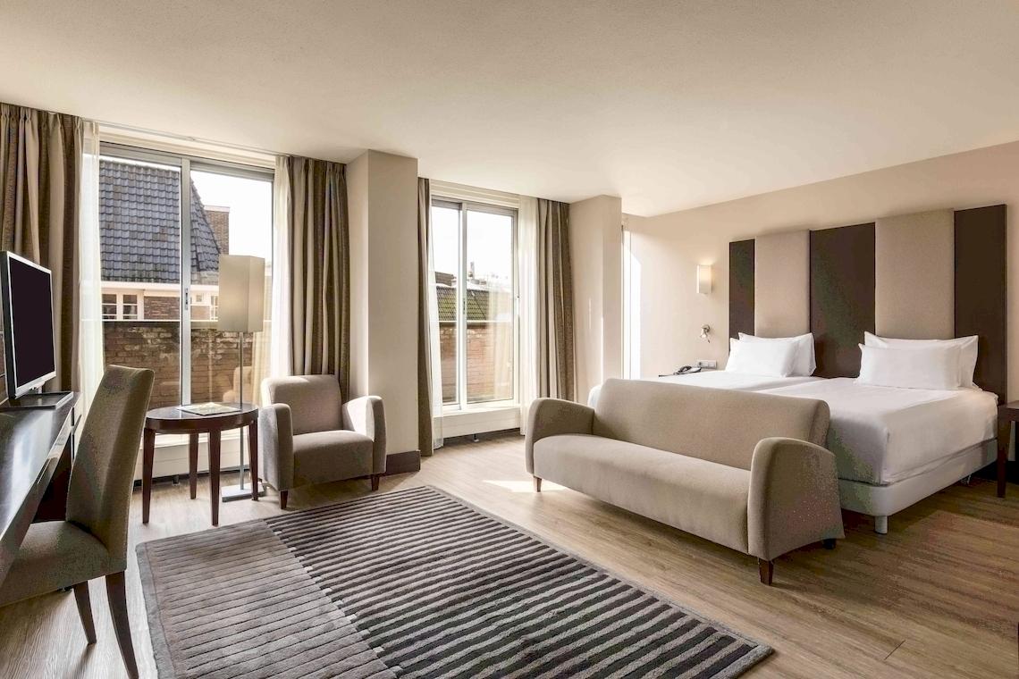 Schlafzimmer im NH Amsterdam Centre Hotel mit Doppelbett, Sofa, Schreibtisch und Fenstern