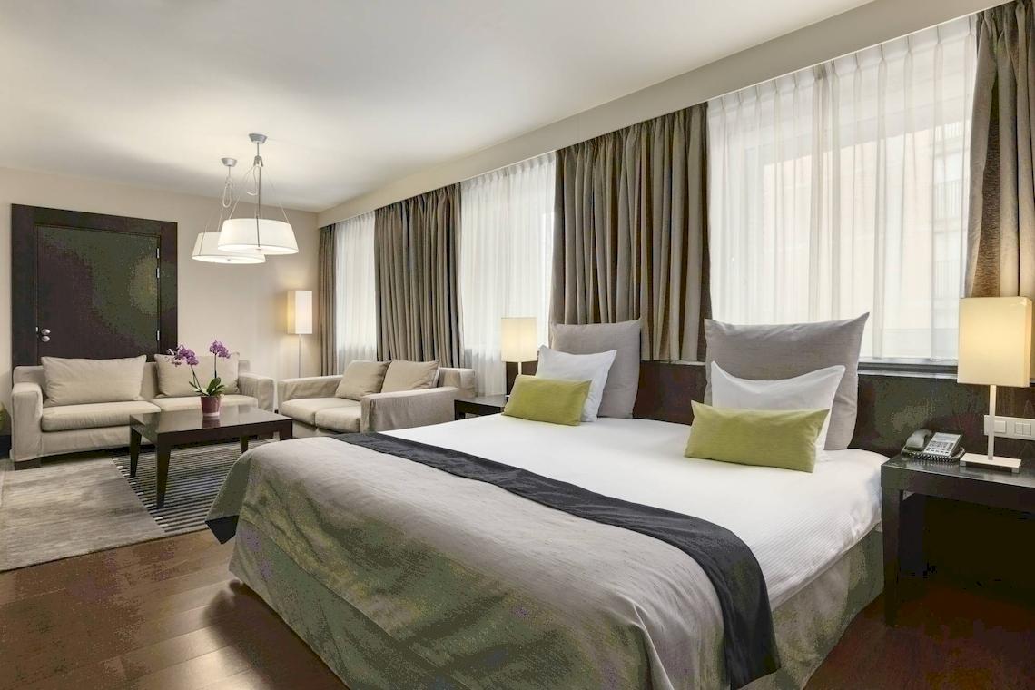 Schlafzimmer im NH Amsterdam Centre Hotel mit großem Bett, Sofas und Nachttischen.