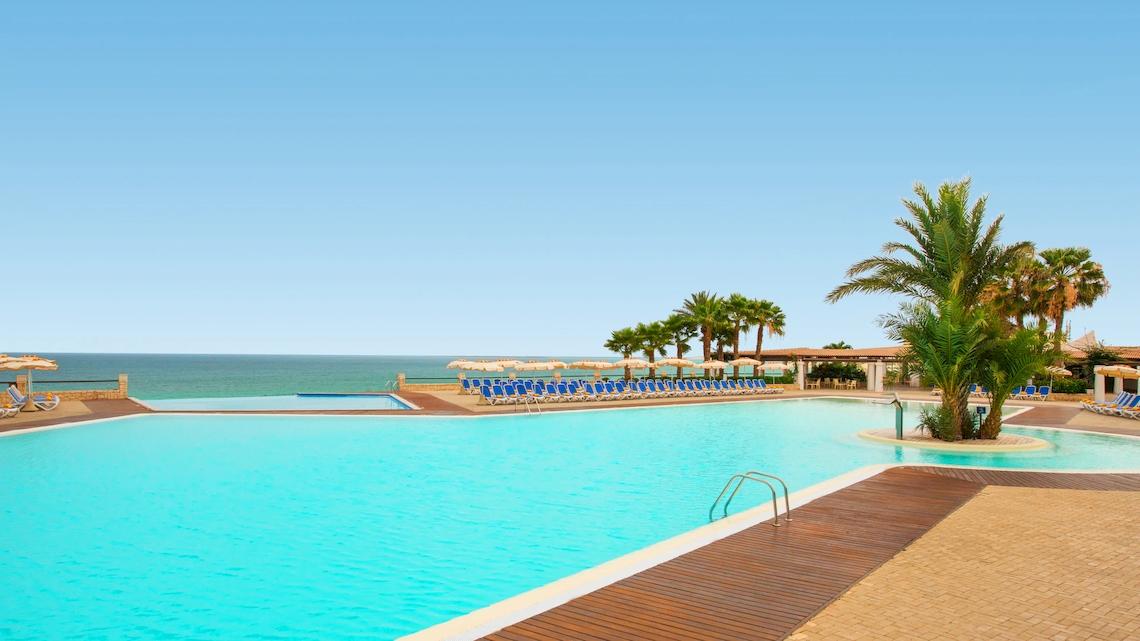 Außenpool des VOI Praia De Chaves Resort mit Blick auf das Meer und Sonnenliegen.