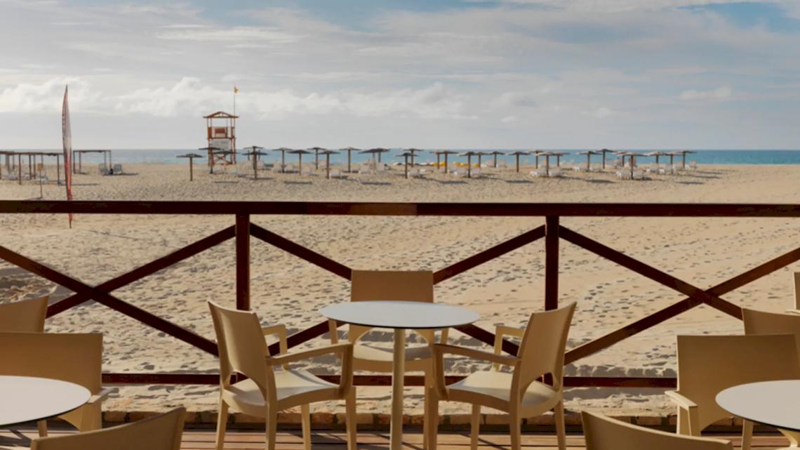 Ausblick auf den Strand des VOI Praia De Chaves Resort mit mehreren Tischen und Stühlen auf der Terrasse.