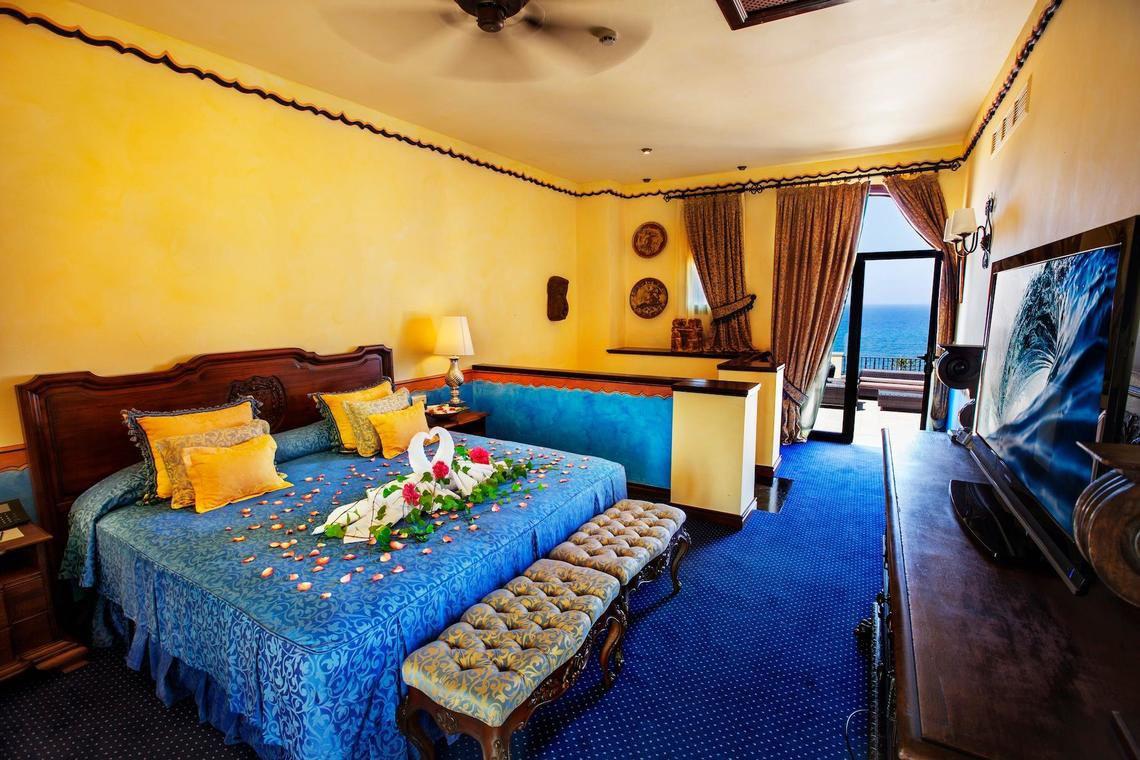 Innenansicht eines Zimmers im Europa Villa Cortes Hotel mit einem großen Bett, dekorativ mit Blumen und einem Ausblick auf das Meer.