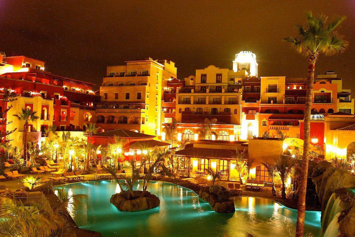 Abendbeleuchtung des Hotels Europa Villa Cortes mit beleuchtetem Pool und Gebäuden.