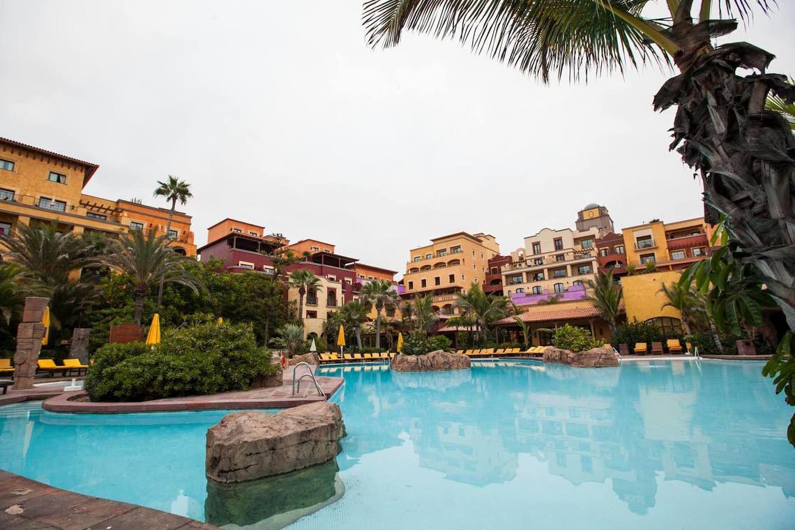 Außenpool des Europe Villa Cortes Hotels mit gelben Sonnenliegen und Gebäuden im Hintergrund.