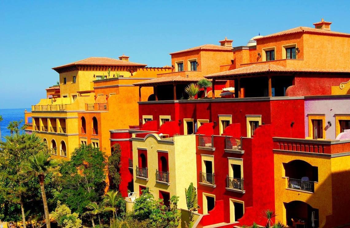 Das farbenfrohe Europa Villa Cortes Hotel mit Blick auf das Meer und umgeben von Bäumen.