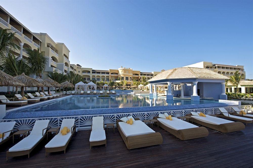 Außenpoolbereich des Iberostar Grand Rose Hall Hotels mit Loungeliegen und Sonnenschirmen.