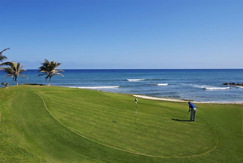 Golfplatz am Strand mit Blick auf das Meer und Palmen, Spieler in Blau.