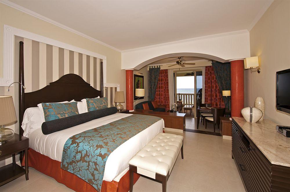 Schlafzimmer im Iberostar Grand Rose Hall Hotel mit Doppelbett, Balkon und Meerblick.