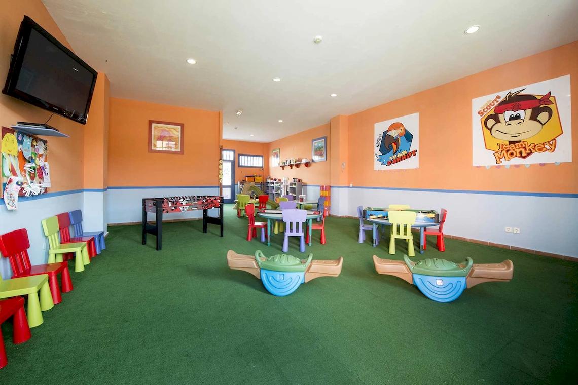 Kinderspielzimmer im Hotel Bahia Principe Sunlight Costa Adeje mit Tischfußball, bunten Stühlen und Tisch, orangefarbene Wände und Fernseher