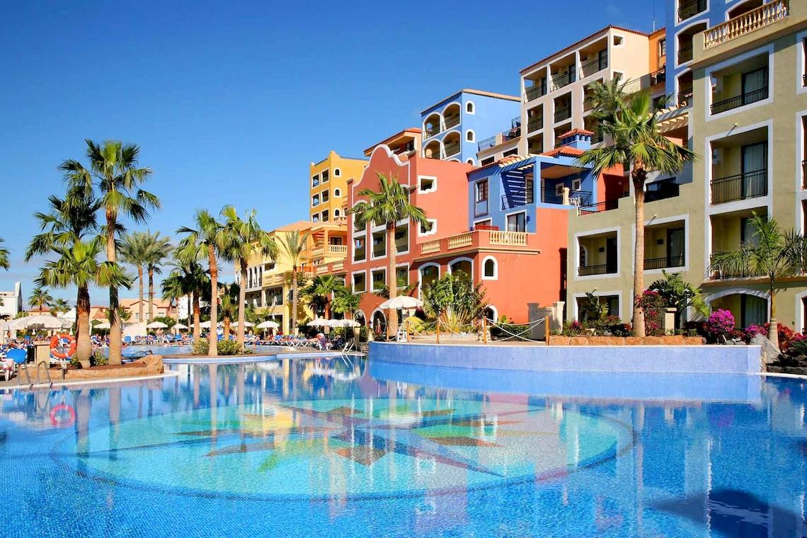 Außenpool des Bahia Principe Sunlight Costa Adeje Hotels mit bunten Gebäuden und Palmen.