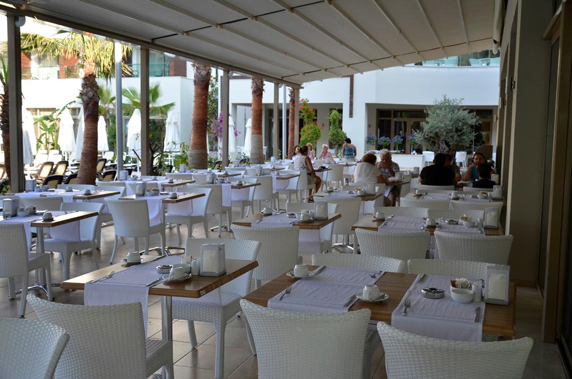 Restaurantterrasse im Port Side Resort mit weißen Tischen und Stühlen.