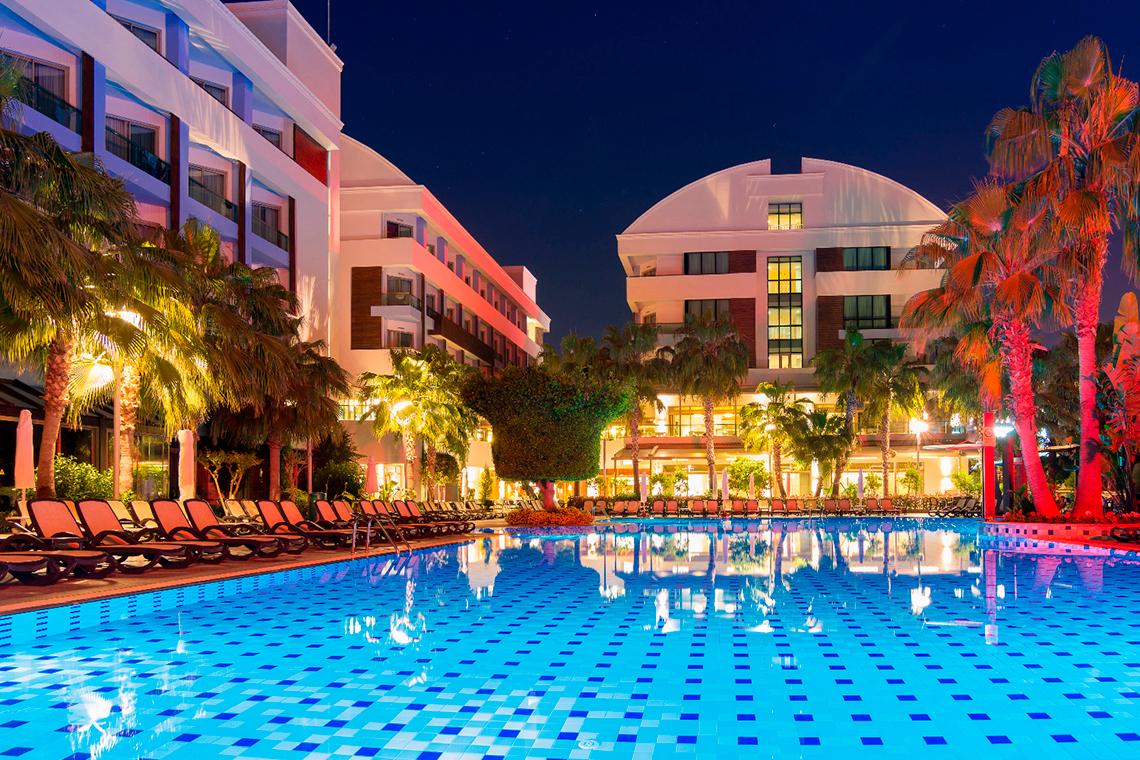 Port Side Resort Pool bei Nacht mit Lounge-Stühlen und leuchtenden Palmen