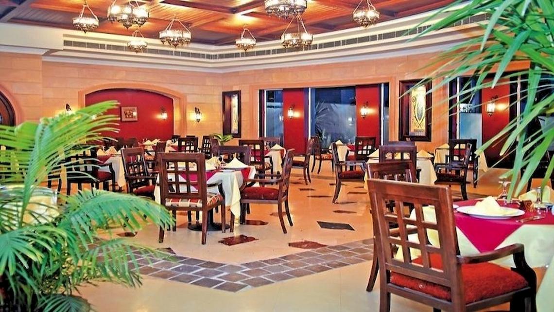 Innenbereich des Serenity Alpha Beach Hotels mit runden Tischen und Stühlen, dekorierten Wänden und Pflanzen.