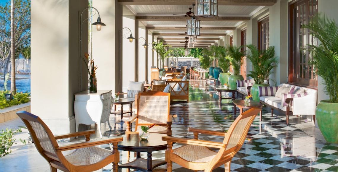 Innenbereich des JW Marriott Mauritius Resorts mit gemusterten Bodenfliesen, Holzstühlen, Tischen, Pflanzen und Deckenventilatoren.