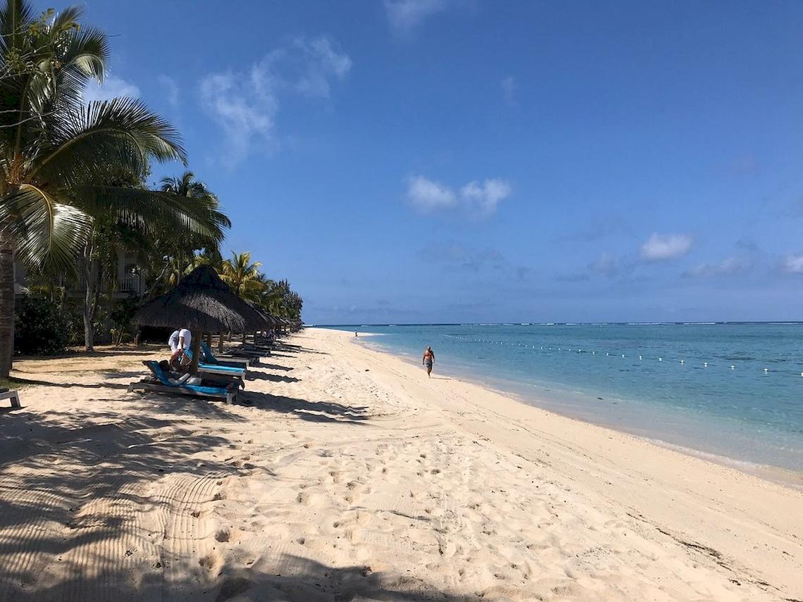 Strand des JW Marriott Mauritius Resorts mit weißen Sand, Palmen und Sonnenliegen.