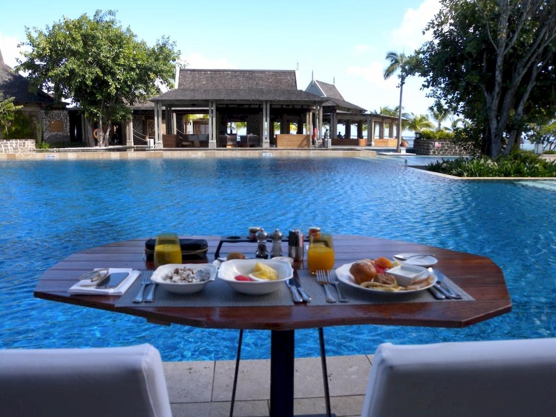 Frühstückstisch am Pool im JW Marriott Mauritius Resort mit Blick auf das Hotelgebäude und den Swimmingpool.