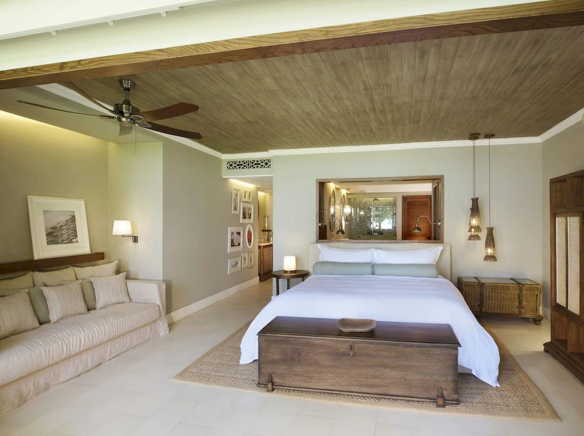 Schlafzimmer im JW Marriott Mauritius Resort mit großem Bett, Sofa, Deckenventilator und Holzmöbeln.
