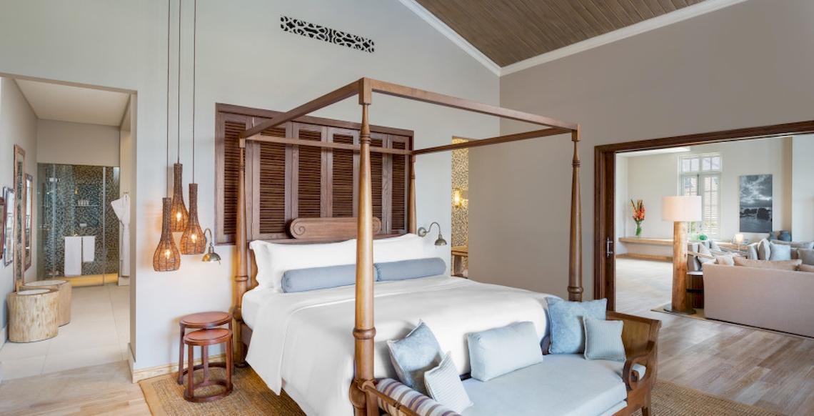 Innenansicht des Schlafzimmers im JW Marriott Mauritius Resort mit einem vierposterbett, hängenden lampen und einem offenen eingang.