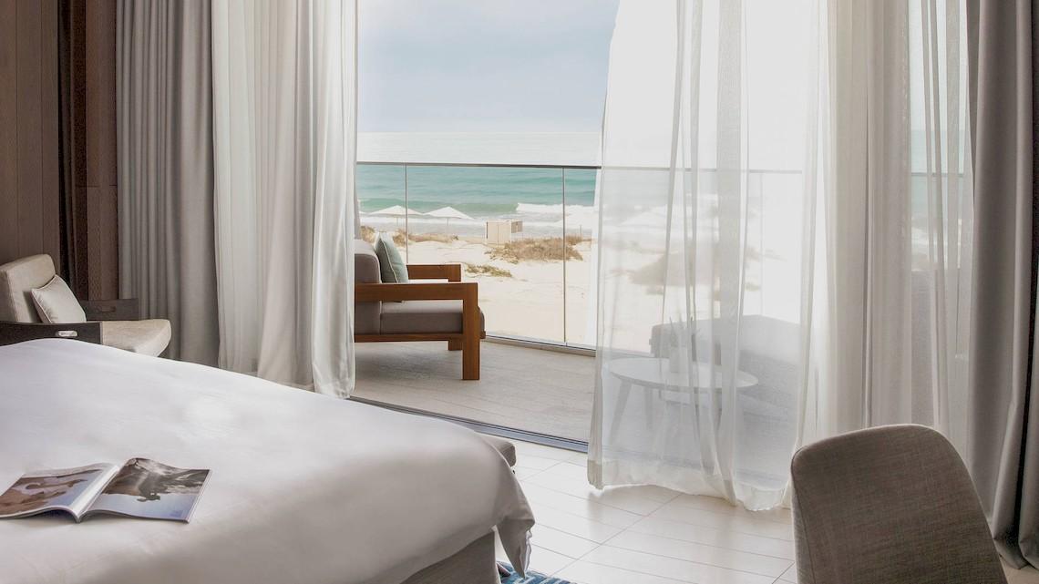 Bett im Hotelzimmer des Jumeirah at Saadiyat Island Resort mit Ausblick auf den Strand.