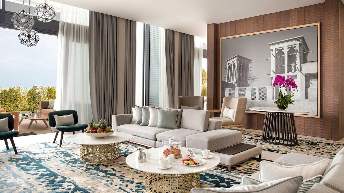 Wohnbereich des Jumeirah at Saadiyat Island Resort mit grauem Sofa, Tisch und Fenster mit Blick auf Bäume.