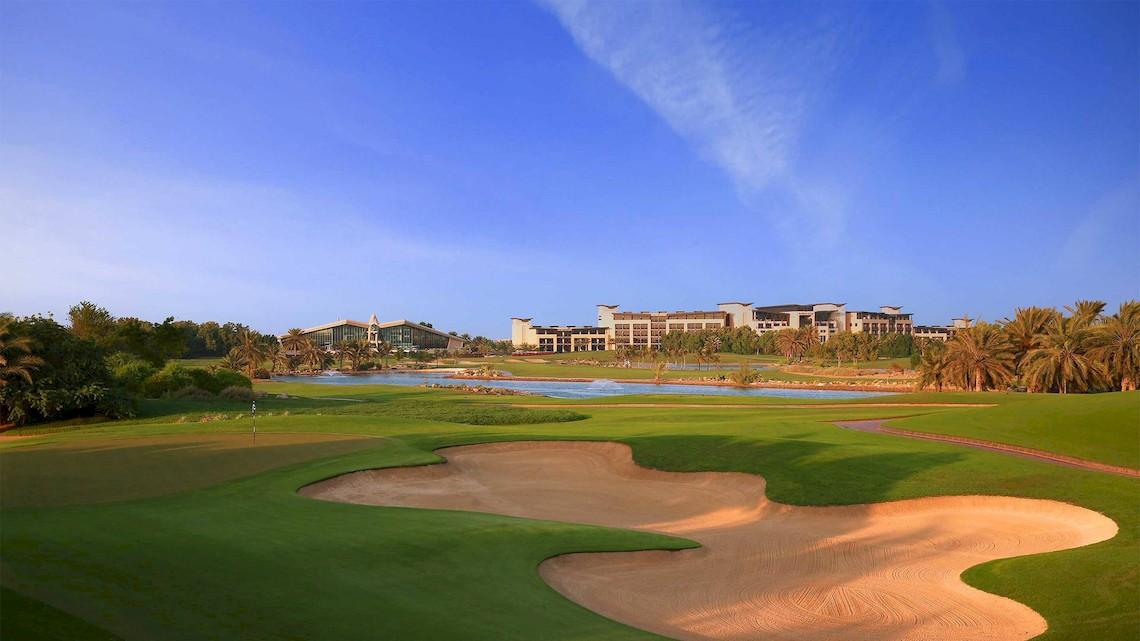 Golfplatz des Jumeirah at Saadiyat Island Resorts mit Wasserhindernis und Hotelgebäude im Hintergrund.