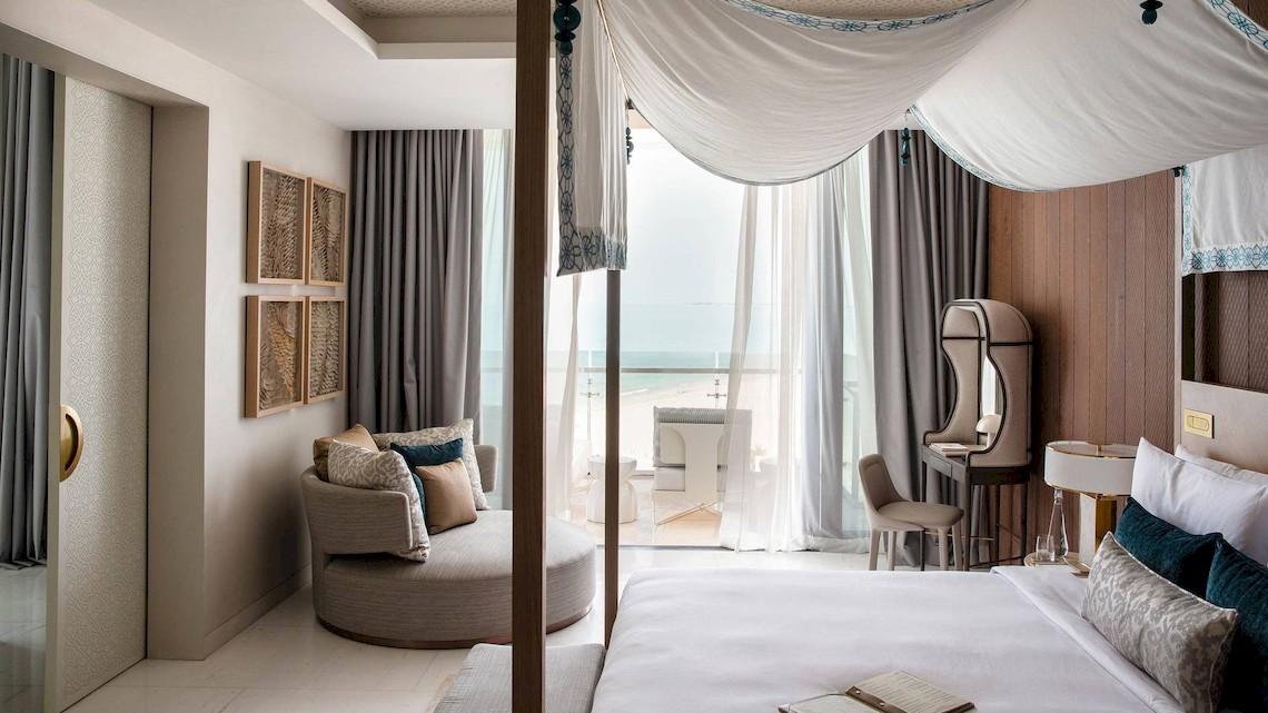 Ein modernes Hotelzimmer mit Aussicht auf das Meer, inklusive eines großen Himmelbetts, einer Sitzecke und einem Schreibtisch.