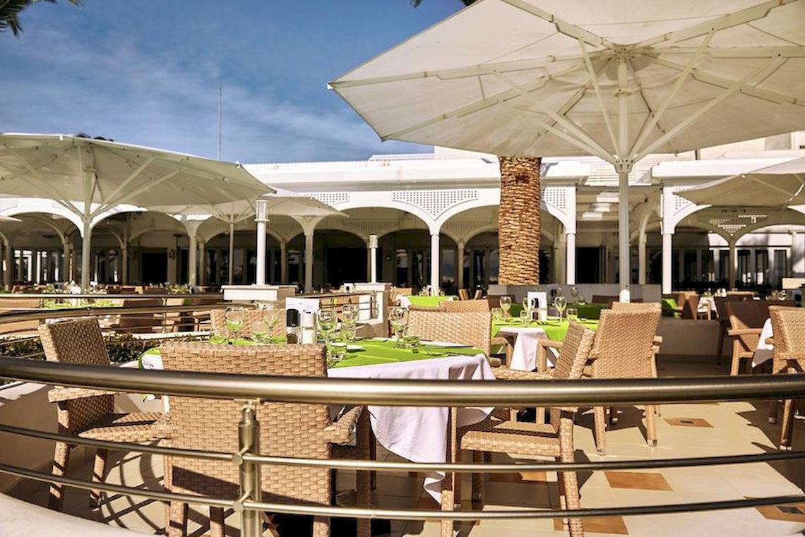 Außenterrasse des Robinson Kyllini Beach Hotels mit Tischen und Stühlen unter Schirmen.