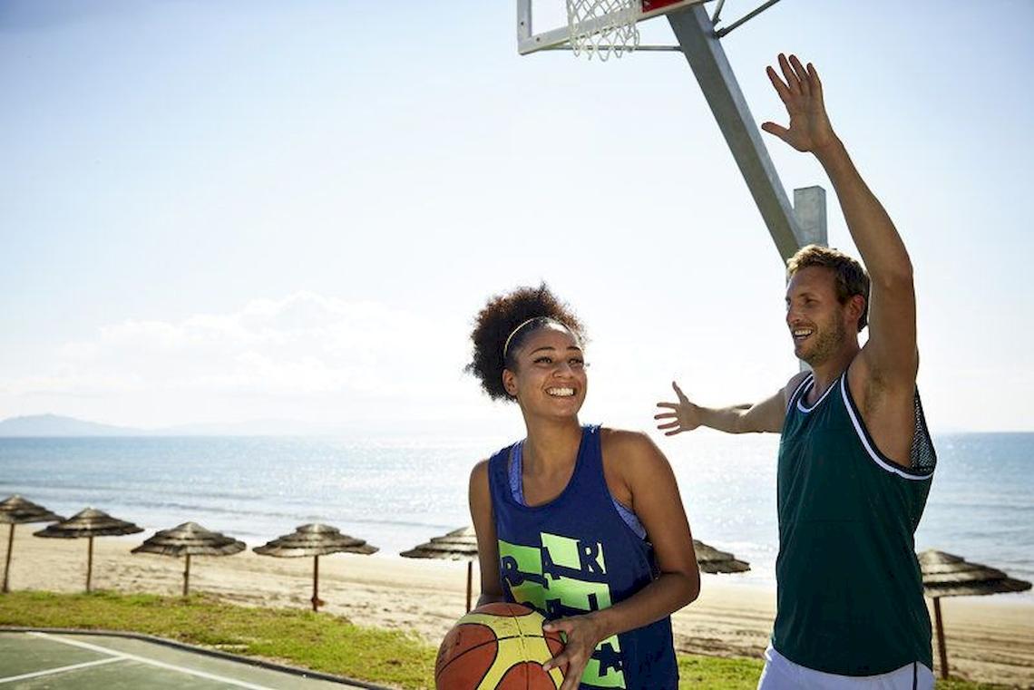 Ein Paar spielt Basketball am Strand mit einer Frau, die den Ball hält, und einem Mann, der nach dem Ball greift.