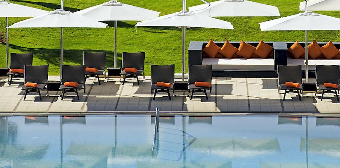 Pool-Loungebereich im Barcelo Palmeraie Hotel mit Sonnenliegen, Kissen und Schirmen.