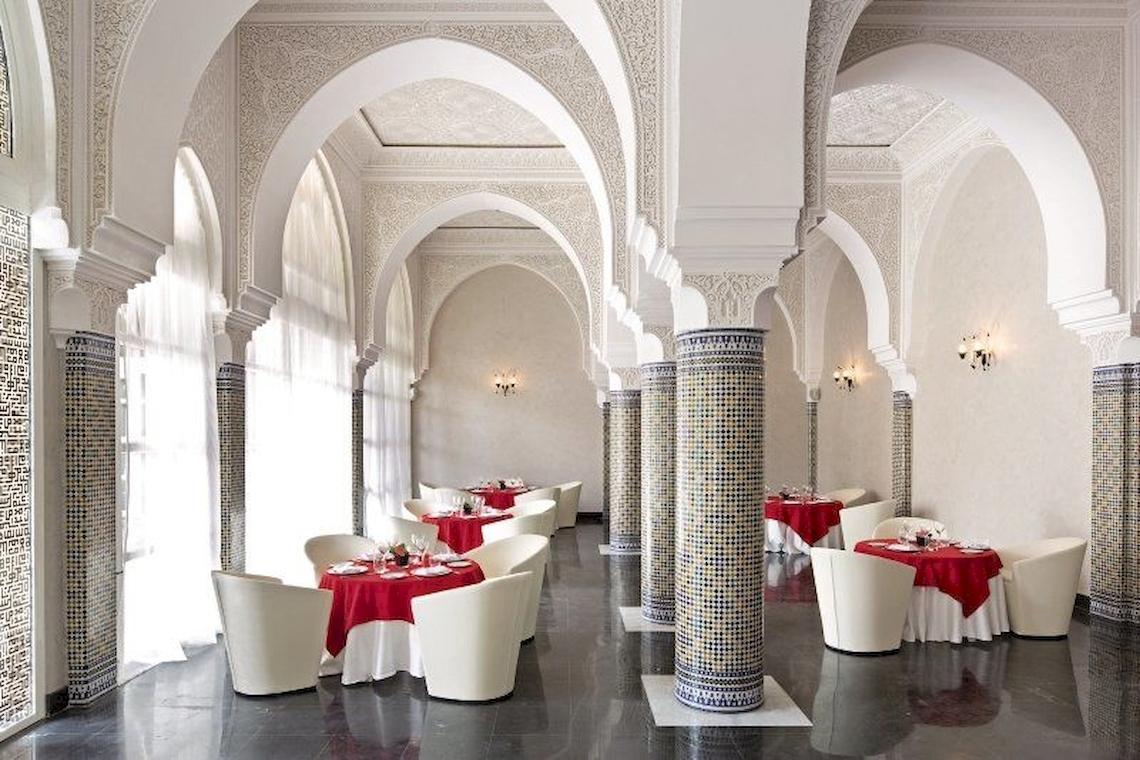 Innenbereich des Barcelo Palmeraie Hotels mit weißer Inneneinrichtung, roten Tischen und Stühlen.