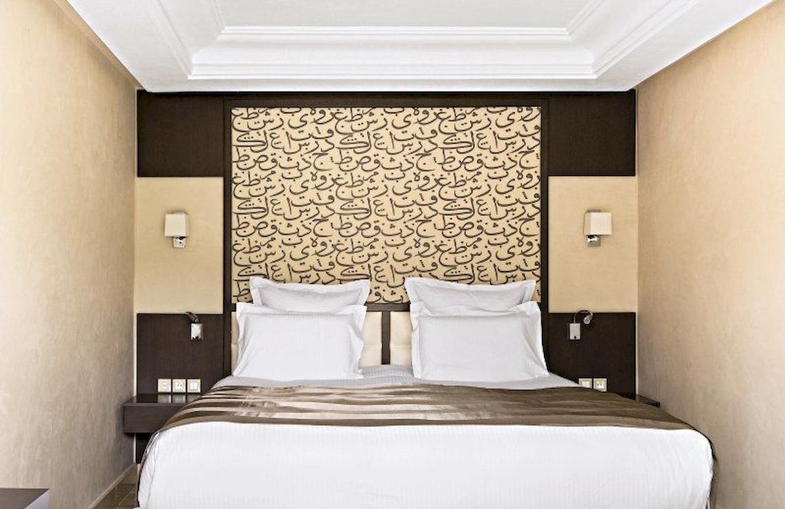 Hotelzimmer im Barcelo Palmeraie mit arabischer Kalligrafie am Kopfende des Bettes.