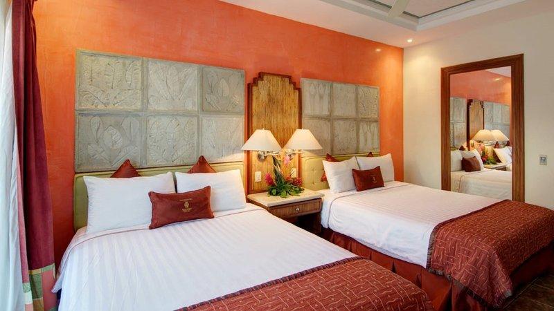 Doppelbettzimmer im Tamarindo Diria Beach Resort mit orangefarbenen Wänden, zwei Betten, Nachttischen und Lampen.