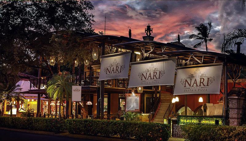 Außenansicht des Tamarindo Diria Beach Resorts mit buntem Himmel und Bannern, die 'Nari Pasta & Pizza' bezeichnen.