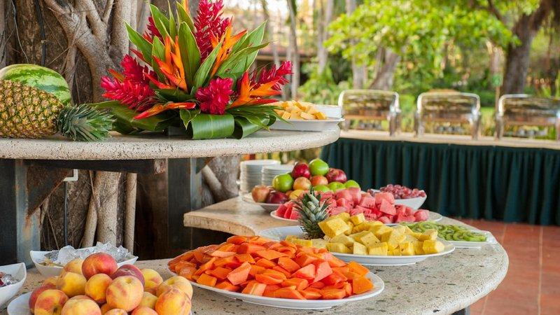 Obstbuffet im Tamarindo Diria Beach Resort mit verschiedenen Früchten und einem Blumenarrangement.