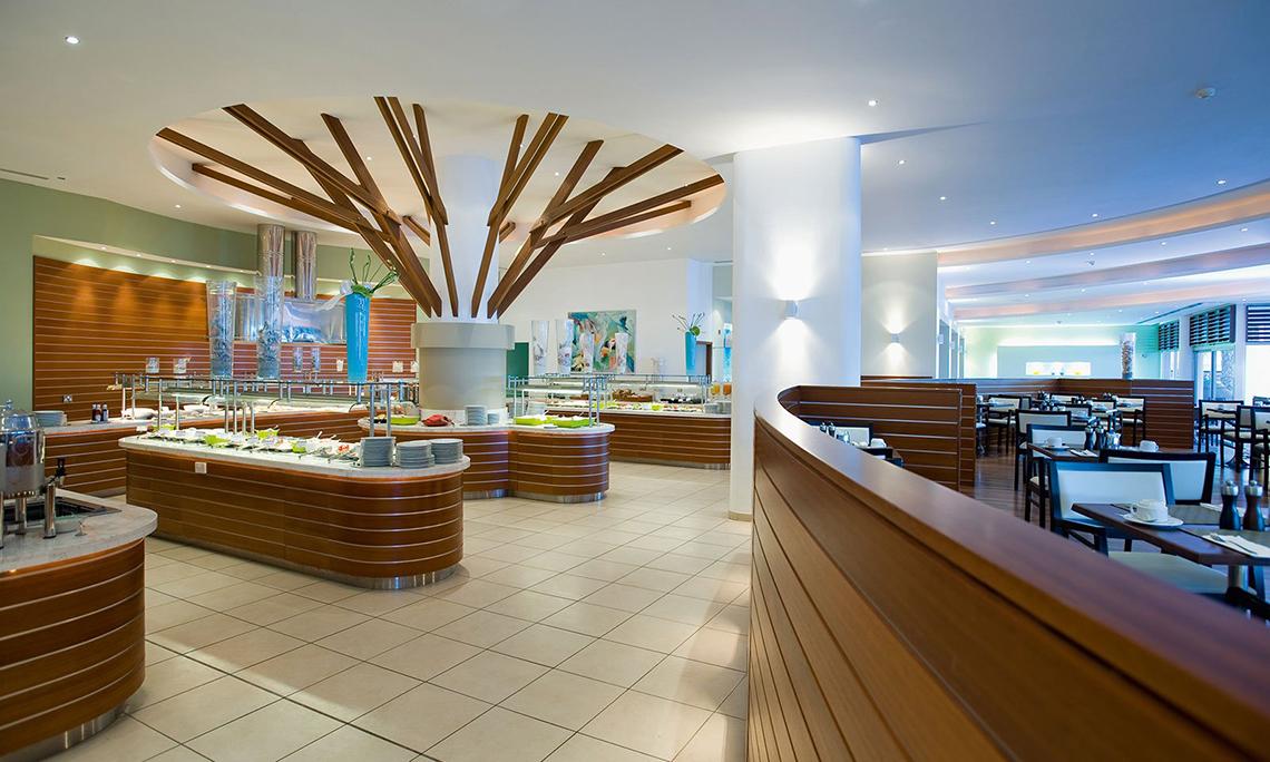 Innenansicht des Restaurants im Mediterranean Beach Hotel in Zypern mit Buffet und Tischen.
