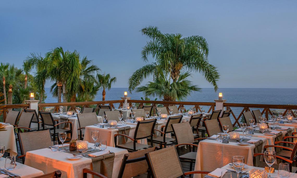 Außenbereich des Mittelmeer-Strandhotels in Zypern mit Tischen und Palmen am Meer