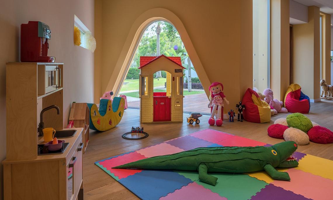 Ein Kinderzimmer mit einer Spielmatte, Spielzeug, einem Haus, Puppen und einer Küche.