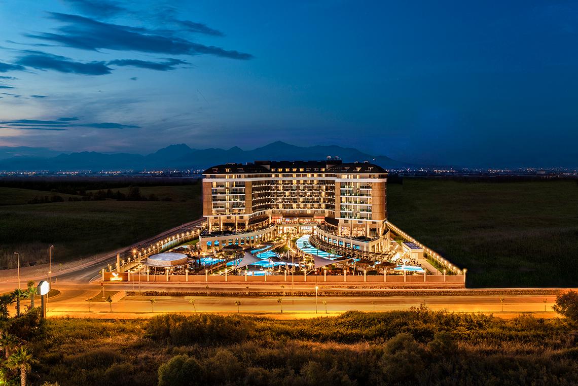 Außenansicht des Aska Lara Resort & Spa bei Nacht mit Beleuchtung und Swimmingpools.