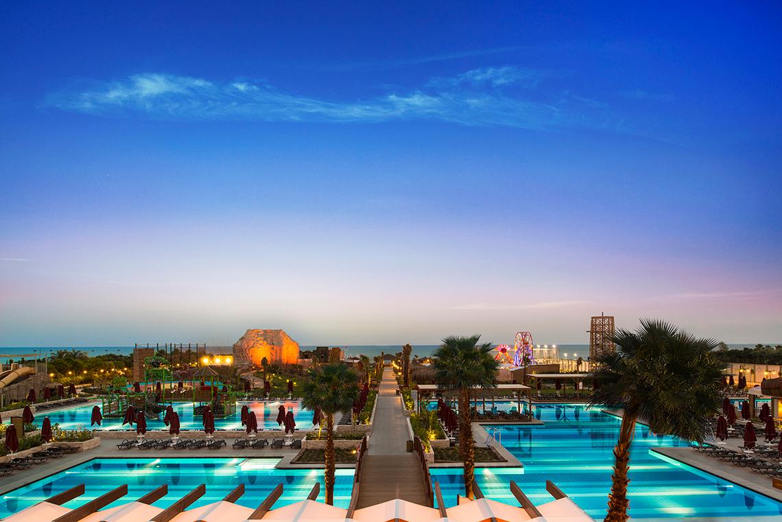 Außenbereich des Aska Lara Resort & Spa am Abend mit Pools und Palmen.